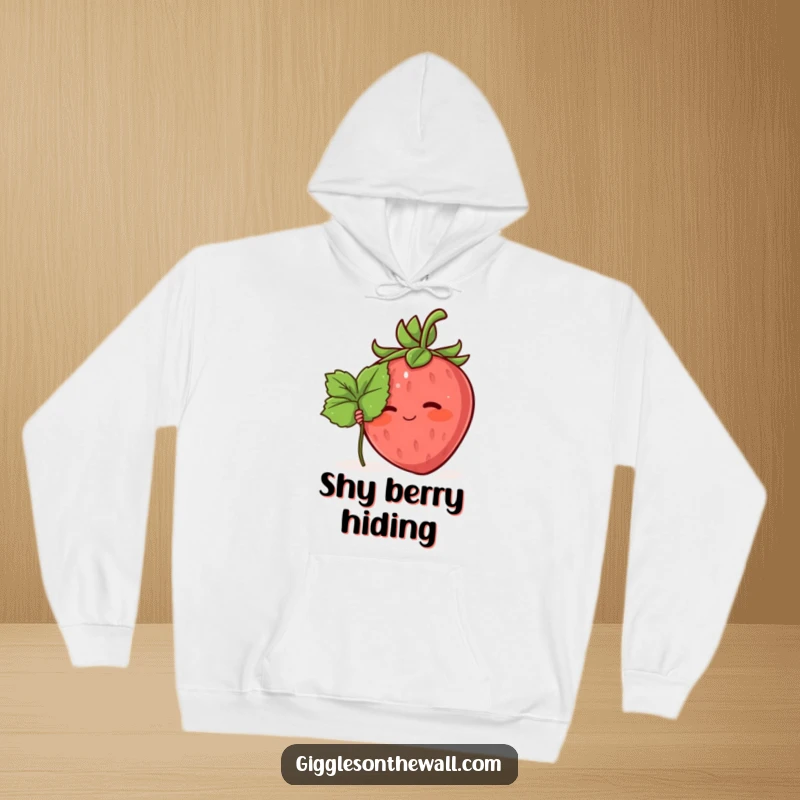 Funny hoodie featuring a blushing strawberry character shyly hiding behind a tiny leaf, offering cozy and endearing humor.